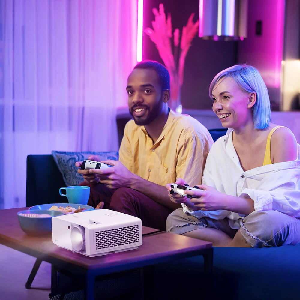 Young couple playing video games with controllers in a dark room using a compact projector — immersive gaming setup with vibrant lighting and enhanced visuals for nighttime play